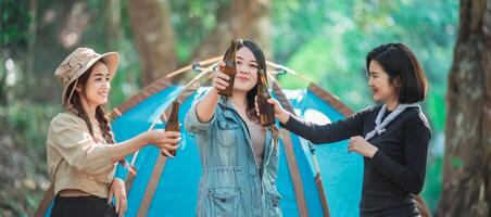 mulheres jovens torcem e bebem bebidas na frente da barraca de acampamento foto