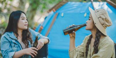 mulheres jovens sentadas e bebem bebidas na frente da barraca de acampamento foto