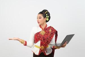 retrato do lindo tailandês mulher dentro tradicional roupas posando com computador portátil computador foto