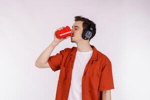 retrato do uma bonito jovem homem com fone de ouvido em pé e bebendo café isolado branco fundo foto