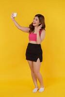 retrato de uma jovem sorridente selfie com o celular nas mãos em pé isolado sobre fundo amarelo foto
