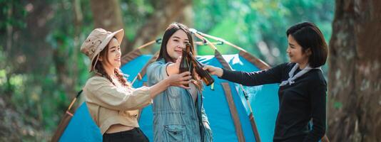 mulheres jovens torcem e bebem bebidas na frente da barraca de acampamento foto