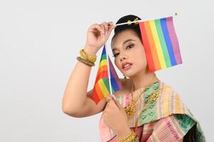 retrato do jovem mulher dentro tailandês nordeste tradicional roupas segurando arco Iris bandeira foto