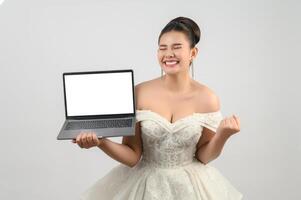 pose de noiva linda jovem asiática com computador portátil de maquete na mão foto