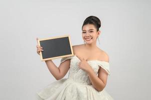 pose de noiva linda jovem asiática com quadro-negro em branco na mão foto