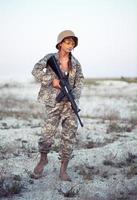 jovem fêmea soldado vestido dentro uma camuflar com uma arma de fogo dentro a ao ar livre foto