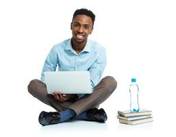 feliz africano americano Faculdade aluna com computador portátil, livros e garrafa do água sentado em branco foto