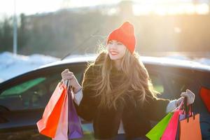 sorridente caucasiano mulher segurando dela compras saco perto a carro foto