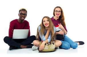 três feliz alunos sentado com livros, computador portátil e bolsas foto