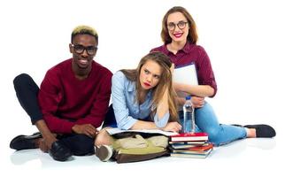 três feliz alunos sentado com livros, computador portátil e bolsas foto