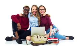 três feliz alunos sentado com livros, computador portátil e bolsas foto