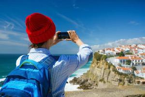 mulher com uma mochila faz uma foto em a Smartphone do uma lindo panorama do a oceano costa perto azenhas Faz mar, portugal