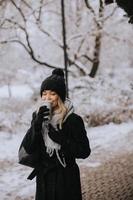 jovem mulher com caloroso roupas dentro frio inverno neve bebendo café para ir foto