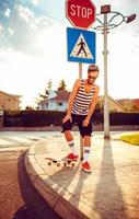 jovem homem dentro oculos de sol com uma skate em uma rua dentro a cidade às pôr do sol luz foto