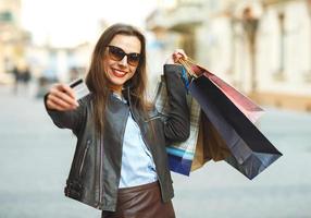 lindo mulher com compras bolsas e crédito cartão dentro a mãos em uma rua foto