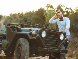 jovem à moda homem com óculos e arco gravata perto a antiquado suv foto