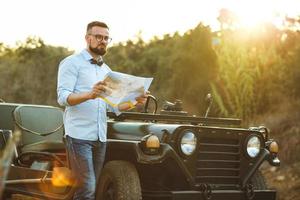 jovem à moda homem com óculos e arco gravata Vejo a mapa perto a antiquado suv foto