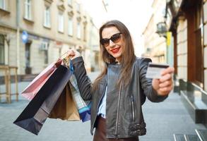 feliz lindo mulher com compras bolsas e crédito cartão dentro a mãos em uma rua foto