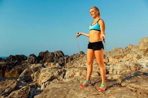 lindo atleta mulher fazendo esporte exercício com a corda em a pedras de a mar foto