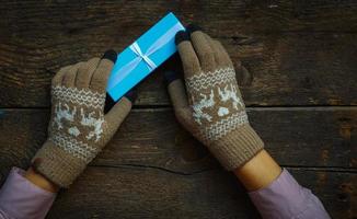 mãos em luvas de inverno com caixa de presente de natal foto