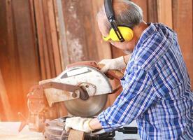 carpinteiro asiático idoso usa serra circular para processar madeira para móveis foto