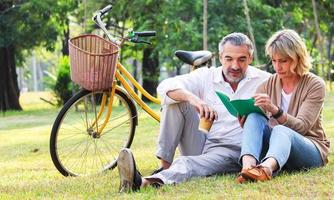 casal feliz sentado no parque com uma bicicleta foto