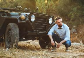 jovem à moda homem com óculos e arco gravata perto a antiquado suv foto