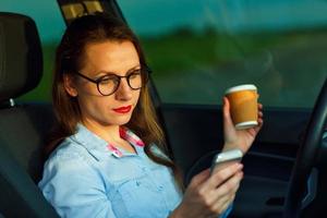 empresária enviando uma texto mensagem e bebendo café enquanto dirigindo uma carro foto