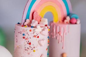 grande bolo de aniversário com arco-íris, granulado colorido. no fundo de muitos balões de coração colorido. festa de aniversário. doce feriado. foto