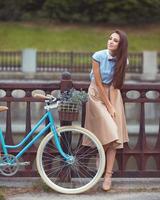 jovem bonita e elegantemente vestida com bicicleta. beleza, moda e estilo de vida foto