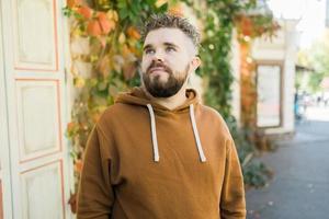 fechar acima tiro do encaracolado europeu masculino com barba desgasta instantâneo ao ar livre. bonito homem com fresco luz cabelo. foto