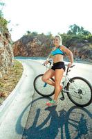 mulher ciclista em pé perto uma bicicleta em uma montanha estrada foto