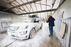 homem lavando carro suv americano de água de alta pressão com rack de teto na lavagem de autoatendimento em clima frio. foto