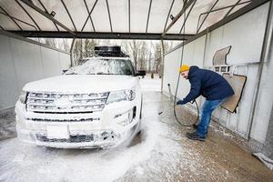 homem lavando carro suv americano de água de alta pressão com rack de teto na lavagem de autoatendimento em clima frio. foto