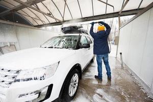homem lavando carro suv americano de água de alta pressão com rack de teto na lavagem de autoatendimento em clima frio. foto
