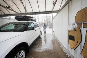 homem lavando carro suv americano de água de alta pressão com rack de teto na lavagem de autoatendimento em clima frio. foto