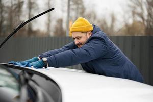 homem limpa o capô do carro suv americano com um pano de microfibra após a lavagem em clima frio. foto