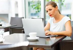 jovem o negócio mulher sentado dentro uma cafeteria com uma computador portátil e café foto