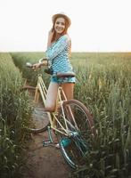 adorável jovem mulher carrinhos dentro uma campo com dela bicicleta foto