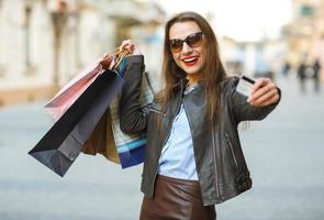 lindo mulher com compras bolsas e crédito cartão dentro a mãos em uma rua foto