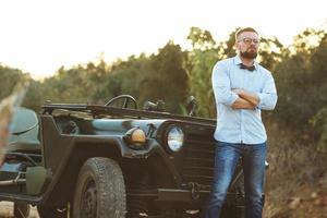 jovem à moda homem com óculos e arco gravata perto a antiquado suv foto