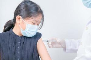 médico injetando vacinação dentro braço do ásia pequeno garota, foto