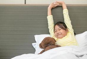 preguiçoso pequeno menina acorda acima e alongamento em cama dentro manhã, saúde Cuidado e Boa manhã foto