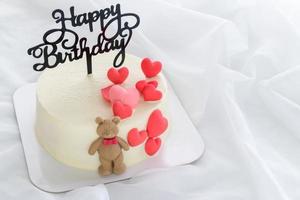feliz nascimento dia fresco manteiga creme bolo decorado com pequeno corações e uma Urso de pelúcia Urso foto