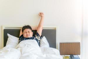 obeso Garoto despertar acima e esticam braço em cama dentro manhã. foto