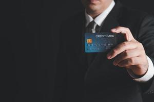 homem de negocios dentro Preto traje e cinzento gravata mostrando crédito cartão foto