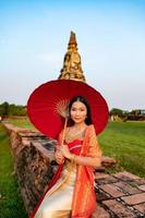 lindo tailandês menina dentro tradicional vestir traje vermelho guarda-chuva Como tailandês têmpora Onde é a público lugar, tailandês mulher dentro tradicional traje do tailândia. foto