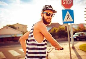 jovem homem dentro oculos de sol equitação uma bicicleta em uma cidade rua às pôr do sol luz foto