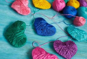 multicolorido corações com uma bolas do fio em azul de madeira fundo foto