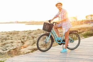 despreocupado mulher com bicicleta equitação em uma de madeira caminho às a mar, tendo Diversão e sorridente foto